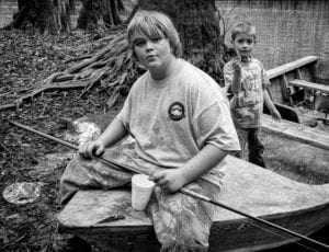 HONORABLE MENTION | Mike Nalley Baiting is an image I made on one of my many trips to Apalachicola Bay to document the oyster and fishing culture. We were at Smith Creek in the Apalachicola National Forest visiting some oystermen and their families on opening day of squirrel season. We found their camp and everyone was enjoying the midday around camp. I just walked around talking and photographing the oystermen and their kids. These two were fishing and playing around the creek when I walked up and got this shot. This is still one of my favorite images made around the bay. BIO: Mike has been photographing since 1974 where it all started as a hobby. He studied photography at the Art Institute of Atlanta where he has an Associate Degree in Photography. He owned and operated a studio in Marietta, GA until 1985 when life got the best of his photography work. Mike became active again in the art world in 2006 when the urge to photograph grabbed him once again. He has worked prolifically in digital ever since. He has spent the last 6 years documenting the oyster and fishing culture in the Apalachicola Bay area of Florida. Over the years he has made some wonderful friends and made some great photographs of the oystermen and women, fishermen and seafood workers in the area. Mike has won many awards over the years. He has exhibited all over the Southeast and can be found most days rambling with his camera in hand in search of that one more subject. ©Mike Nalley